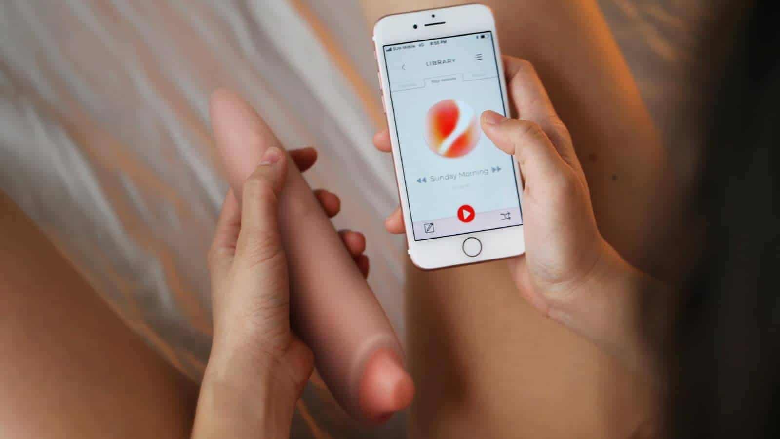 A woman using a cell phone to play with a smart oral sex toy.